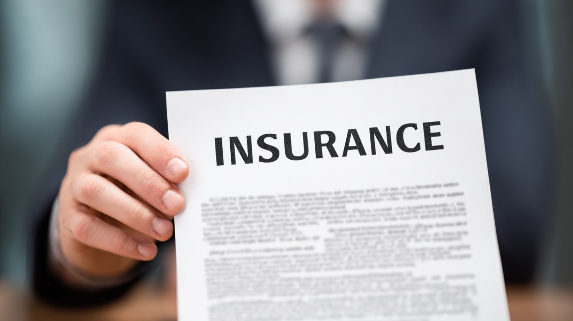 Person in a suit holding a document labeled “INSURANCE,” symbolizing reviewing policy details
