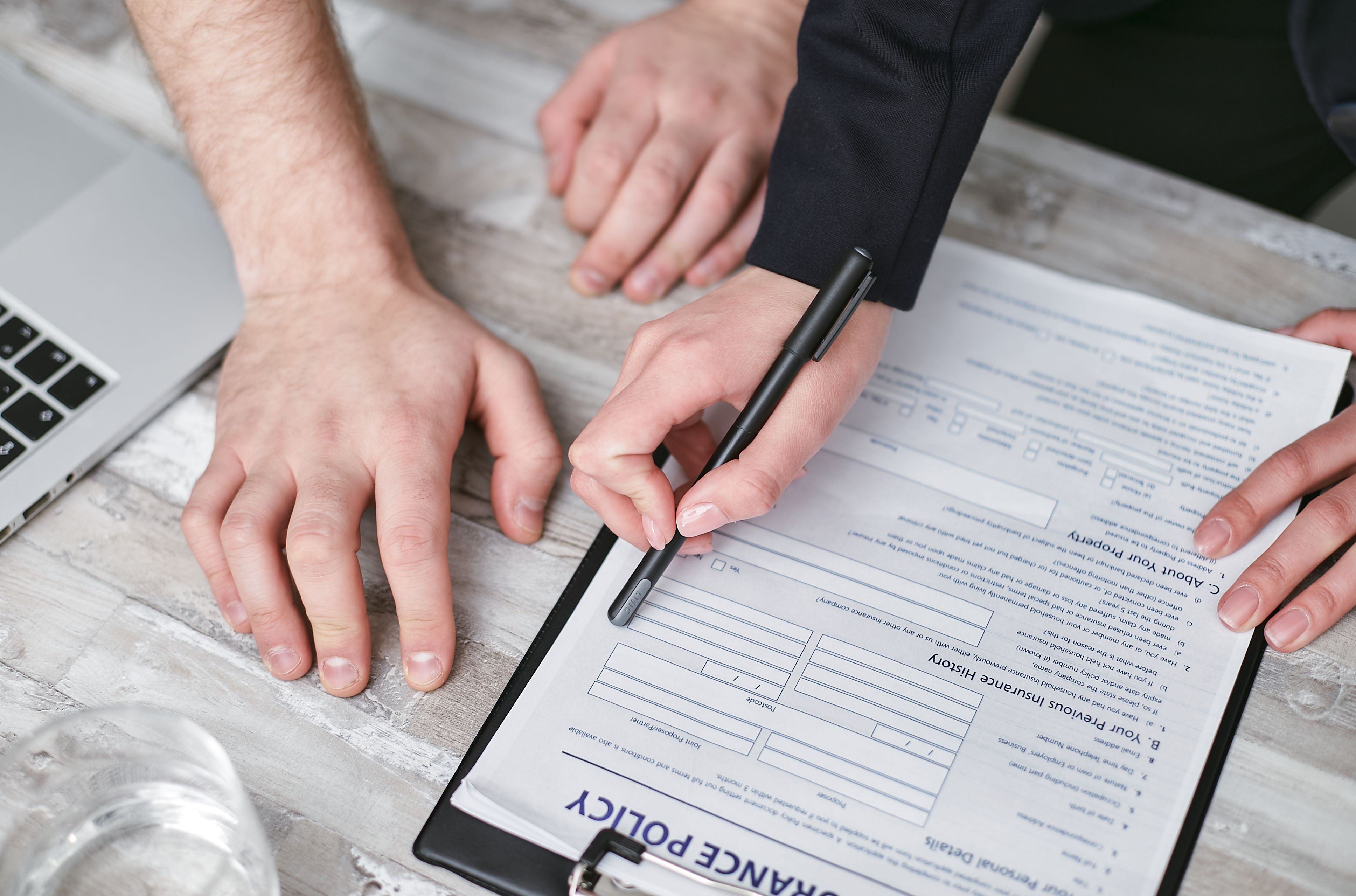 Two people signing a travel insurance policy document at a wooden desk