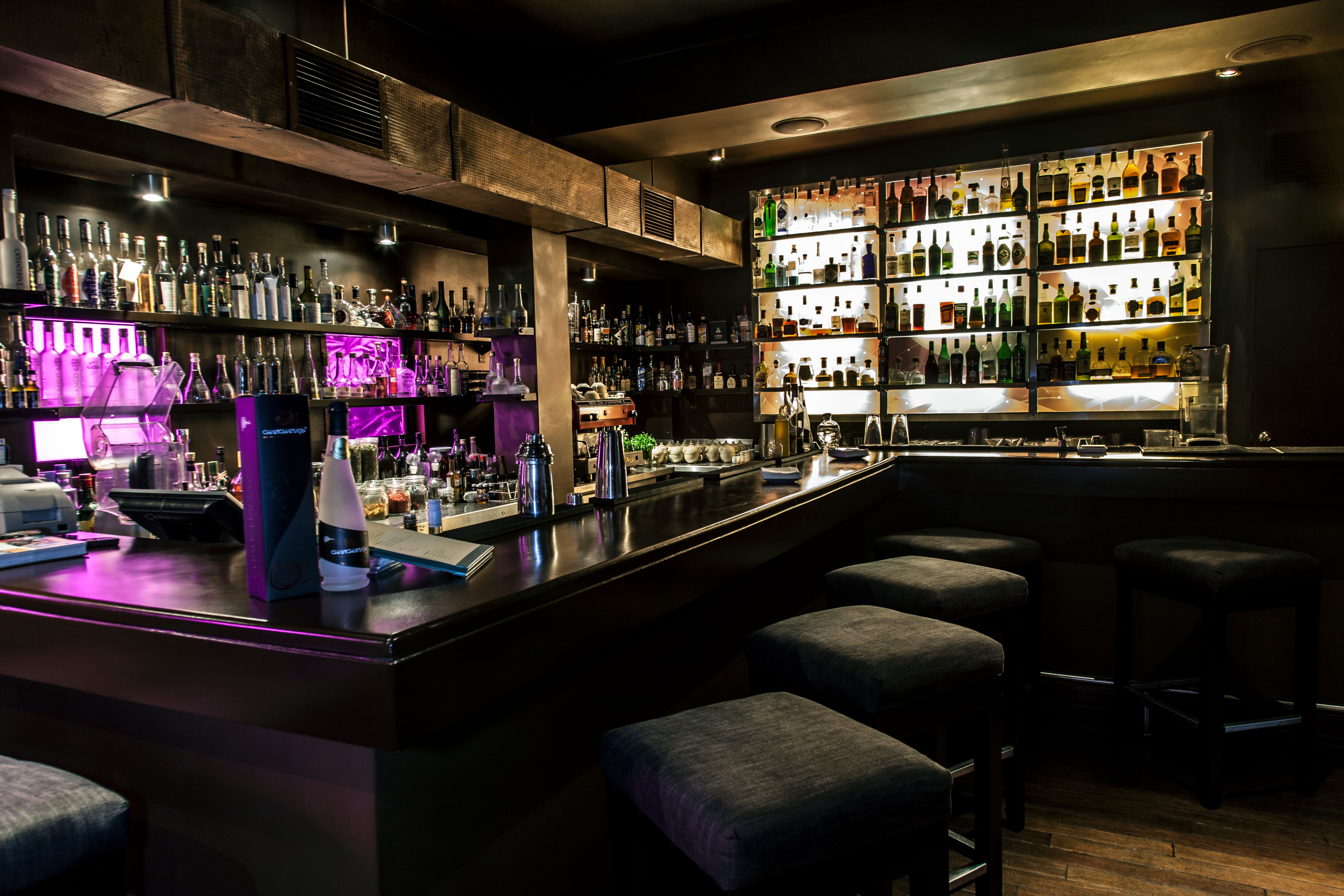 Stylish cocktail bar with illuminated bottle shelves and intimate ambient lighting.